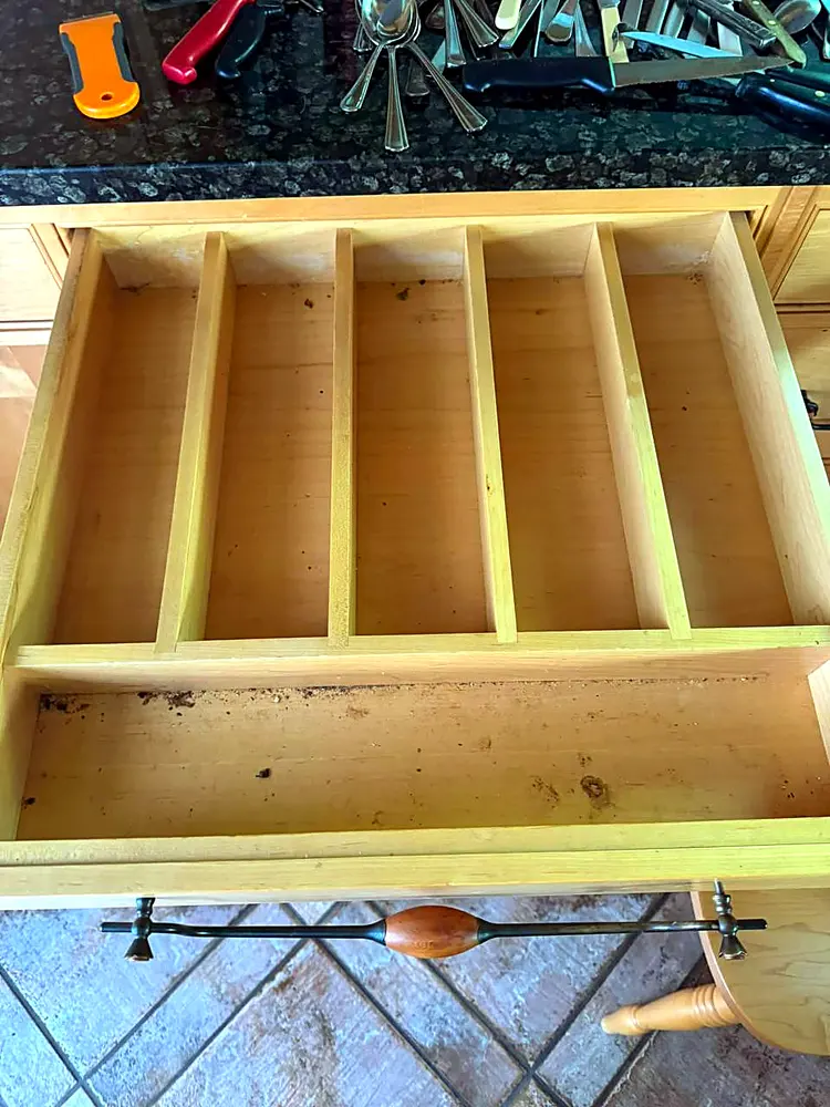 Cutlery drawer with crumbs and debris in the bottom before cleaning